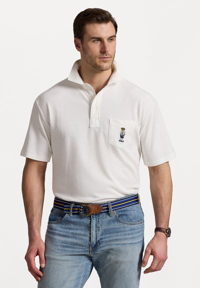 Tricou polo alb cu guler, mâneci scurte și buzunar la piept decorat cu un logo brodat. Purtați cu blugi din denim albastru și o curea cu dungi.