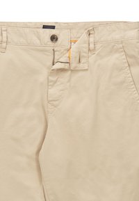 Beige bomullbyxor med dragkedja och knappstängning. Utrustad med fickor och en sömnadsdesign. Slät textur, vanlig passform.