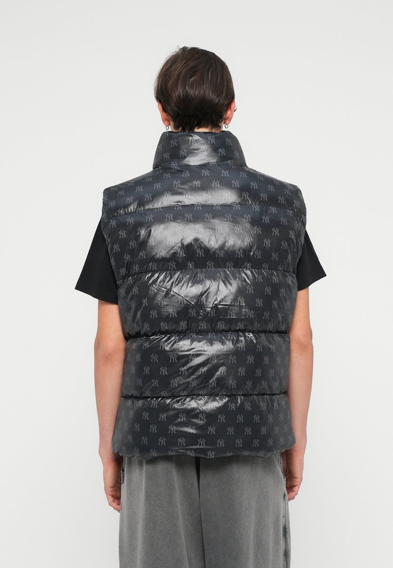 Puffy, sleeveless vest in glossy black material with gray repeating logo pattern, high collar, and quilted sections. No visible fastenings.