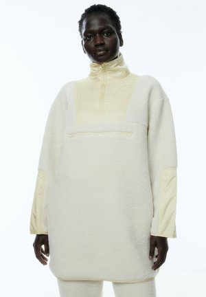 Witte fleece trui met een hoge kraag, contrasterende crème panelen en een ritszak aan de voorkant, met een zachte textuur en een oversized pasvorm.