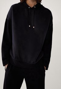 Zwarte hoodie met een ontspannen pasvorm, gemaakt van zachte stof. Voorzien van koordjes en een geribbelde onderrand. Geen zichtbare patronen of accenten.