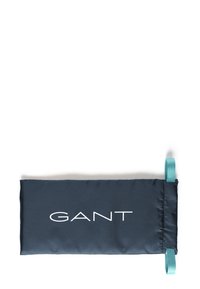 Bolsa de tela de color azul marino con acabado mate, que presenta un logo blanco de "GANT". Incluye una cinta de color teal para facilitar su transporte o sujeción.