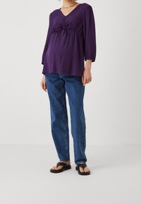 Lila långärmad blus med V-ringning, smal midja och avslappnad passform, kombinerad med blå raka jeans och svarta flip-flops.