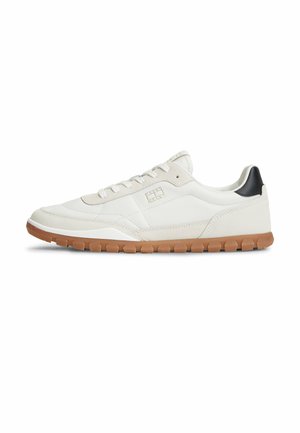 Hvid lavskoet sneaker med beige accenter, gummisål, snørelukning og sort hælfane, vist i sideprofil på hvid baggrund.
