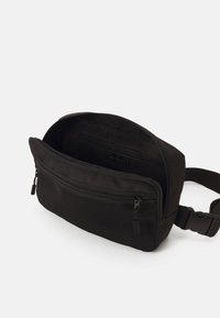 Borsa a tracolla nera in tessuto con scomparto principale con zip, tasca anteriore e tracolla regolabile. Superficie testurizzata e hardware resistente.