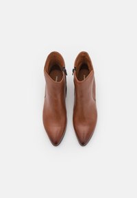 Paire de bottines en cuir marron avec des bouts pointus et des fermetures éclair latérales, vues de dessus sur un fond blanc.