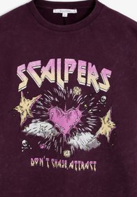 Tricou din bumbac maro roșcat cu un design grafic care include textul „SCALPERS”, o inimă roz, cranii și modele explozive. Guler rotunjit, mâneci scurte.