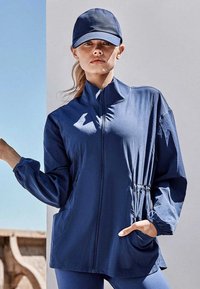 Lichtgewicht jack in marineblauw met een hoge kraag, ritssluiting, elastische taille en zijzakken, gecombineerd met een bijpassende pet.