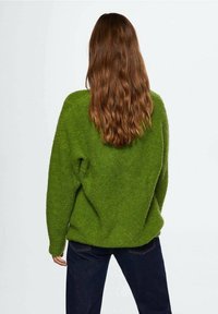 Pull vert surdimensionné en tissu duveteux avec une coupe décontractée, présentant un matériau texturé et des épaules tombantes. Associé à un jean en denim foncé.