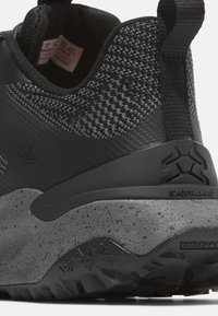 Černá atletická bota s texturovaným svrškem, šedou skvrnitou mezipodešví, silnou oporou paty a gumovou podrážkou s vzorovaným perfilováním.
