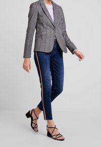 Grå randig blazer över en ljuslila topp, matchad med mörkblå jeans med siddragkedja och svarta remsandaler.