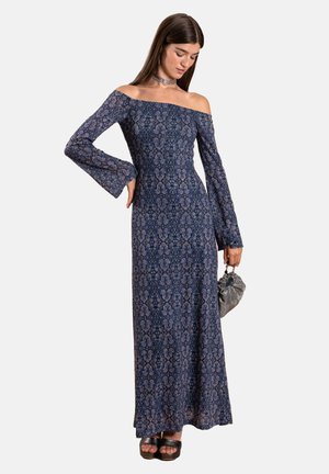 Langes, schulterfreies Kleid in Marineblau mit Blumenmuster, mit weit ausgestellten Ärmeln und einer figurbetonten Silhouette. Kombiniert mit einer kleinen grauen Handtasche und schwarzen Schuhen.