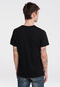 Black cotton t-shirt with short sleeves and crew neck, featuring a smooth texture and a straight hem, worn with blue jeans.