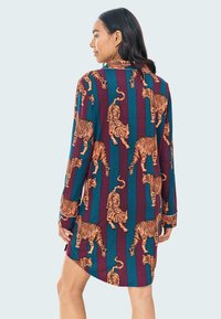 Camicia a maniche corte con un motivo di tigre multicolore su uno sfondo a righe bordeaux e teal, dotata di colletto e polsini con bottone.