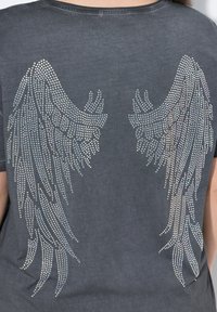 Grå T-shirt med et glitrende stempel af vinger på bagsiden. Stoffet ser blødt ud med en afslappet pasform og en let struktureret overflade.