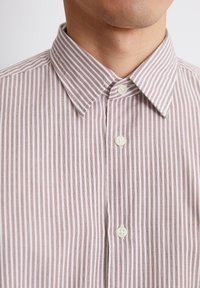 Camicia a righe con bottoni, caratterizzata da sottili linee verticali in rosa pallido e bianco. Design con colletto, bottoni standard e una texture liscia.