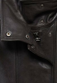 Close-up van een zwart leren jas met metalen drukknoopsluitingen, rits en gedetailleerde stiksel.