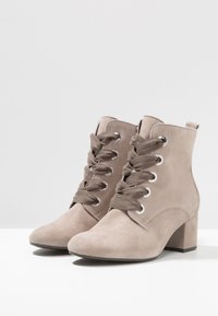 Botas de tobillo de ante beige con punta redonda, cordones en la parte delantera y ojales plateados, con un tacón grueso y una textura suave.