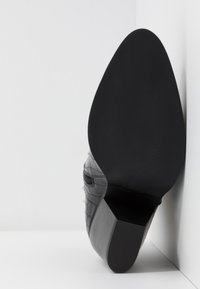 Chaussure à talon noire avec une tige en cuir texturé effet crocodile, un bout pointu et une semelle en caoutchouc lisse avec un léger motif de crantage.