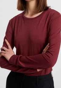 Bordeaux lange mouwen shirt met een ronde halslijn, gemaakt van zachte stof. Kenmerkt zich door strakke mouwen en een gladde textuur, gedragen met zwarte broek.