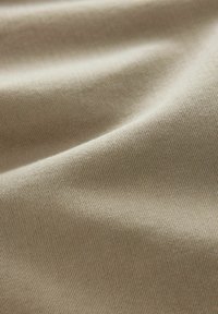 Beige struktureret stof, der viser en glat overflade med et subtilt vævet mønster, draperet for at fremhæve dets bløde og lette egenskaber.