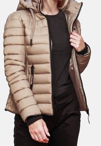 Beige pufferjakke med vandret polstring, lynlås foran og hætte. Sorte ærmer og sidelommer tilføjer kontrast og funktionalitet.