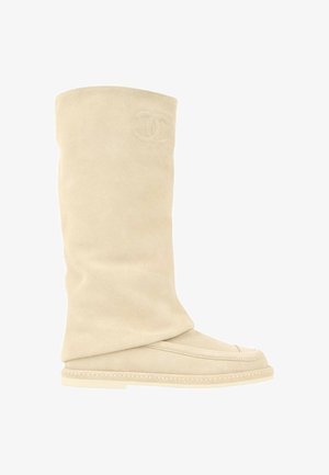 Botte beige en daim mi-mollet avec semelle plate et logo brodé près du haut sur fond blanc.