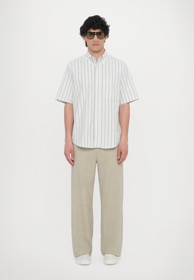 Knappskjorte med hvite og lysegrå striper, kombinert med beige vide bukser og hvite sneakers. Modell som har på seg oversized solbriller.