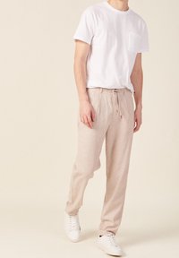 T-shirt en coton blanc avec une poche sur la poitrine, associé à un pantalon en lin beige avec une taille élastique et un cordon de serrage. Porté avec des baskets blanches.