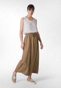 Falda de longitud media en color beige, con cintura ajustable mediante cordón, combinada con una blusa sin mangas blanca y zapatillas de lona beige. Tela suave, corte relajado.