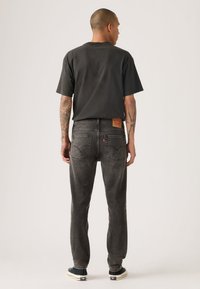 Μαύρο κοντομάνικο μπλουζάκι συνδυασμένο με σκούρο γκρι τζιν παντελόνια που διαθέτουν δερμάτινο λογότυπο και ορατές ραφές, εμφανιζόμενο από πίσω.