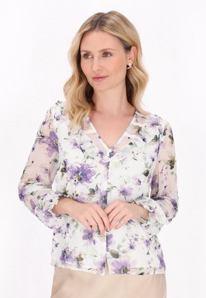 Camicia trasparente con bottoni e motivo floreale in viola e verde, collo arricciato e maniche lunghe con polsini elasticizzati.