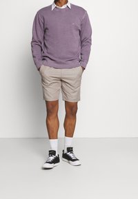 Felpa lilla, camicia bianca con colletto sotto, pantaloni corti beige e scarpe da ginnastica nere con suole bianche, indossate con calzini bianchi alla caviglia.