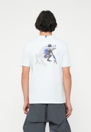 Lyseblå bomulds T-shirt med et geometrisk design af en frø og menneskefigurer på ryggen. Korte ærmer og rund halsudskæring.