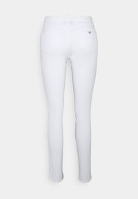 White skinny jeans with a smooth texture, featuring a mid-rise waist, two back pockets, and a small logo accent on the waistband.