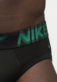 Κοντινό πλάνο ενός ατόμου που φοράει μαύρα boxer Nike με ευρεία μαύρη και πράσινη μέση που διαθέτει το λογότυπο Nike και ένα μικρό πράσινο σήμα στο πόδι.