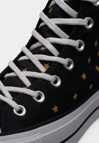 Μαύρο υψηλό αθλητικό παπούτσι με λευκά κορδόνια, ασημένιες τρύπες, λευκή ελαστική σόλα και χρυσό αστέρι σε σχέδιο πάνω στο ύφασμα.