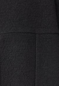 Černá texturovaná látka s měkkým, filcovým povrchem. Vyznačuje se čistými švy, které zajišťují hladký, rovnoměrný vzhled. Bez viditelných vzorů nebo akcentů.