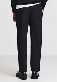 Schwarze Hose aus glattem Stoff, mit geradem Schnitt, Gesäßtasche mit Knopfdetail und minimalistischem Bunddesign.