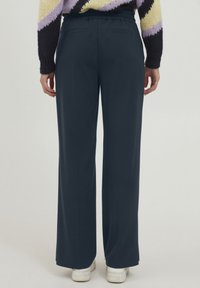 Navy wijde broek met een elastische tailleband, voorzien van twee achterzakken en een gladde textuur, gecombineerd met witte sneakers.
