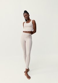 Světle béžová sportovní souprava obsahující zkrácený top a legíny s vysokým pasem. Ozdobena kontrastním žlutým šitím. Hladká textura.