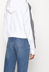 Vit cropped hoodie med huva och svarta sidostråk, kombinerad med högmidjade blå denimjeans med bakfickor och en avslappnad passform.