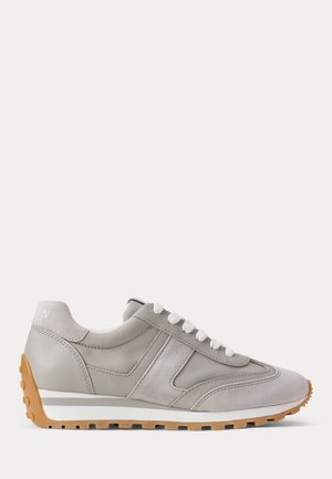 Zapatilla casual gris clara con cordones blancos y suela de goma, costuras detalladas y superposiciones texturizadas en el lateral y la zona de los dedos.