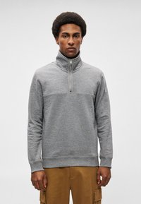 Γκρι φούτερ με μισό φερμουάρ και ψηλό γιακά, με υφασμάτινη υφή και αντιθετικό κάτω τμήμα. Συνδυασμένο με χακί cargo παντελόνι.