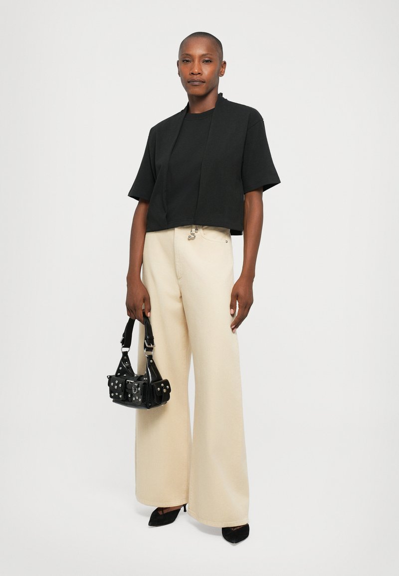 Black cropped top with short sleeves, beige wide-leg pants, and a small black handbag featuring silver accents. Smooth textures throughout.