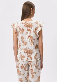 Biała bluzka z pomarańczowym wzorem kwiatowym, falbaniastymi rękawami i teksturowanym materiałem, zestawiona z pasującymi spodniami w ten sam wzór.