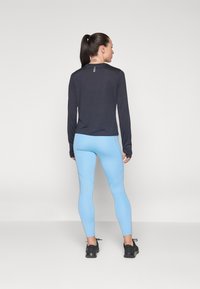 Top oscuro de manga larga con acentos reflectantes, combinado con leggings ajustados de color azul claro que presentan cortes y paneles texturizados, usados con zapatillas negras.