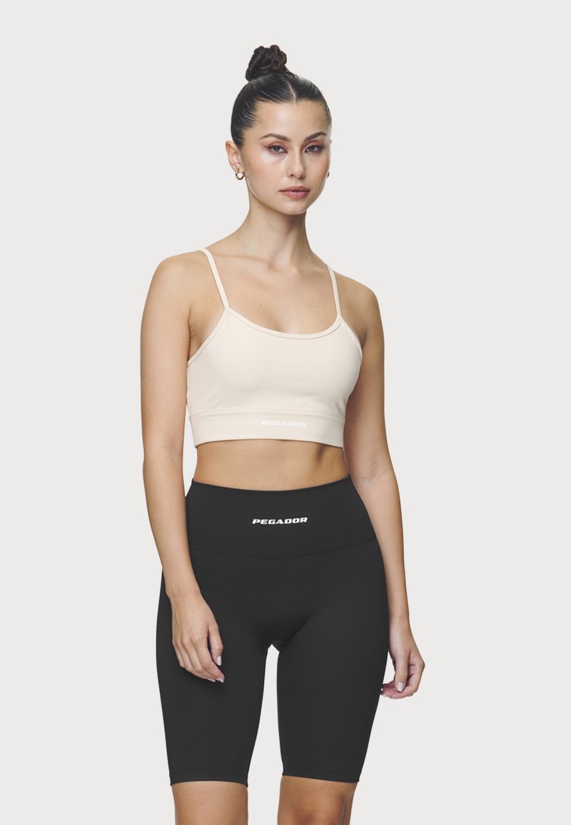 Sujeción deportiva rosa claro con tirantes finos y logotipo. Pantalones cortos de ciclismo negros de cintura alta con logotipo. Tejido suave y elástico, silueta ajustada.
