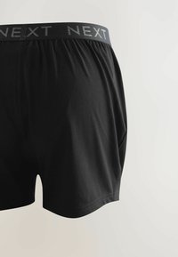 Schwarze Baumwoll-Boxershorts mit einem weichen Bund und dem "NEXT"-Logo. Die Shorts haben einen lockeren Schnitt und eine glatte Textur.
