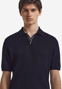 Marineblå kortärmad polo t-shirt med en strukturerad stickad design, med en dragkedjeöppning och kontrasterande sträck i halslinningen.